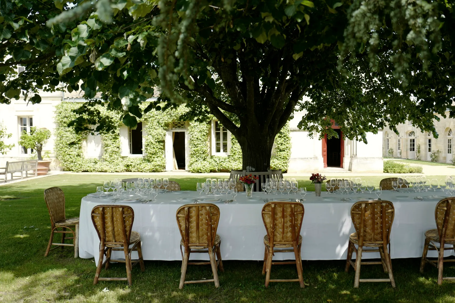 Table de réception dressée à l’ombre d’un arbre devant une demeure en pierre