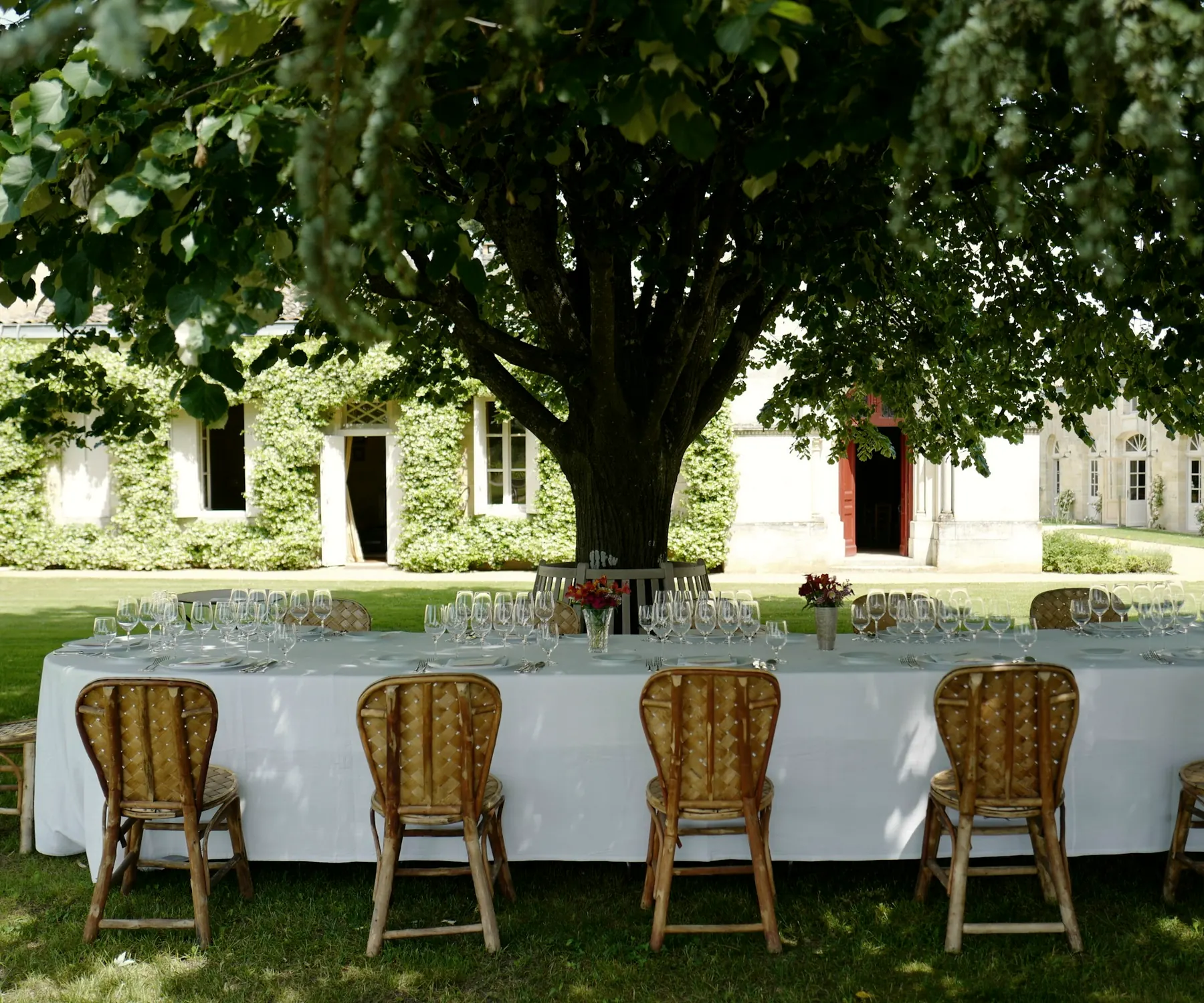 Table de réception dressée à l’ombre d’un arbre devant une demeure en pierre